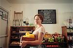 Portrait of female shop assistant carrying fruit and veg crate in country store