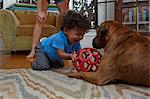 Male toddler playing with dog on sitting room floor