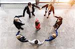 Overhead view of business team in circle holding hands surrounding boss