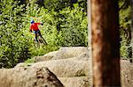 Young female bmx biker jumping mid air from rocks in forest