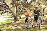 Mature couple chatting and pushing bicycles through park