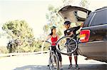 Mature couple removing bicycles from car boot in park