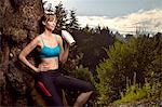 Female runner leaning against rock in park drinking water