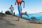 Mid adult man and young giving running on path by sea, rear view