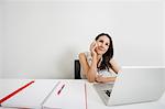 Smiling businesswoman looking away while answering cell phone at desk in office