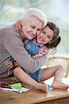 Portrait of senior woman hugging granddaughter sitting on table at home