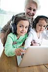 Portrait of happy senior woman with granddaughters listening to music while using laptop