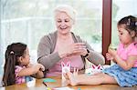 Senior woman assisting granddaughters in art work at home