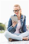 Full length of young female college student using tablet PC in park