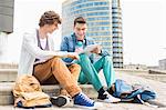 Full length of young male college students studying on steps against building