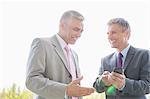 Happy businessmen discussing over mobile phone outdoors