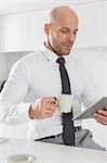 Mid adult businessman having coffee while using tablet PC in kitchen