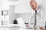 Mid adult businessman using laptop at kitchen counter