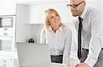 Happy business couple working on laptop in kitchen