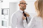 Woman adjusting businessman's tie at home