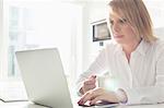 Beautiful mid adult businesswoman using laptop while having coffee at home