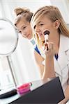 Girl watching sister applying makeup in front of mirror at home