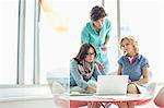 Businesspeople using laptop at table in creative office