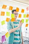 Smiling businessman reading sticky notes on glass wall in creative office