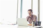 Mid-adult businessman using laptop at desk in creative office