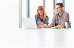 Business colleagues using laptop at desk in creative office