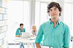 Portrait of confident businessman with colleagues working in background at creative office