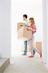 Full-length side view of couple walking with cardboard boxes