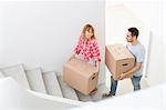 Happy couple carrying moving boxes up stairs in new house