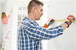 Man measuring wall with woman painting in background