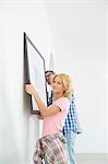 Couple hanging picture frame on wall in new house