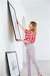 Woman hanging picture frame on wall in new house