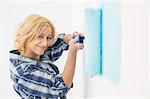 Portrait of beautiful woman painting wall with paint roller