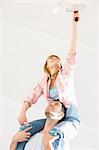 Woman on man's shoulders painting ceiling with paint roller