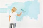 Rear view of woman painting wall with paint roller