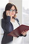 Portrait of smiling businesswoman using cell phone while holding file in office