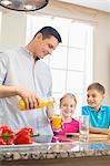 Father serving orange juice for children in kitchen