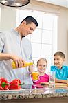 Father serving orange juice for children in kitchen