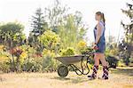 Full-length side view of female gardener pushing wheelbarrow at plant nursery