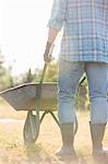 Low section rear view of man pushing wheelbarrow at garden