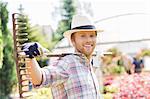 Portrait of smiling gardener carrying rake on shoulders at plant nursery