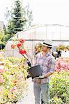 Male gardener looking at flower pot outside greenhouse