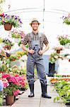 Full-length portrait of happy gardener standing at greenhouse
