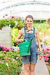 Portrait of happy female gardener holding watering can in greenhouse