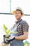 Portrait of happy gardener holding potted plant at greenhouse