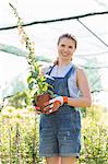 Portrait of happy gardener holding potted plants at greenhouse