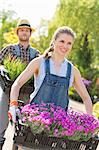 Smiling gardeners carrying flower pots in crates at plant nursery