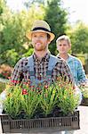 Male gardeners carrying flower pots in crates at plant nursery