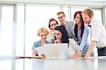 Business colleagues with laptop analyzing document in creative office