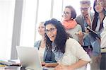 Group of cheerful businesspeople with laptop at desk in creative office