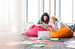 Creative businesswomen using tablet PC while relaxing on beanbag chairs at office